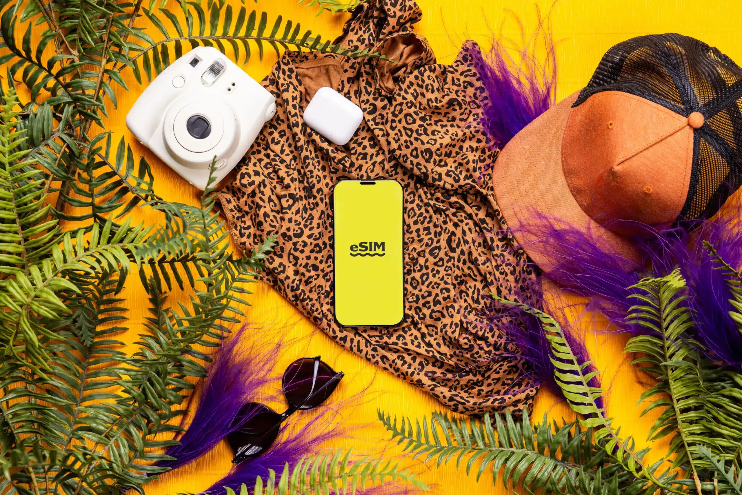 Accessoires de voyage d'été avec un smartphone affichant une eSIM internationale, un appareil photo instantané et une casquette